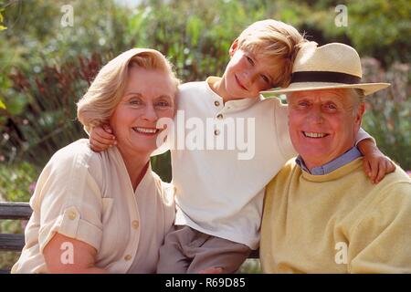 All'aperto, Ritratto, 6 Jahre alter blondr Junge zwischen seinen auf einer Parkbank sitzenden Grosseltern Foto Stock