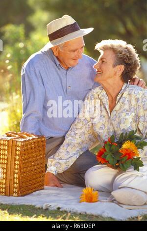 Ritratto, all'aperto, Profil, Seniorenpaar Mitte 60 sitzt mit Picknickkorb und einem Strauss Blumen auf einer Wiese im Sommer Foto Stock