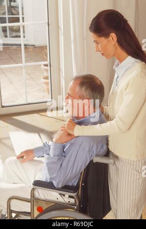 Ritratto, Innenraum, Halbfigur, Frau mit langen Haaren braunen schiebt ihren im Rollstuhl sitzenden Vater vor eine Glastuer Foto Stock