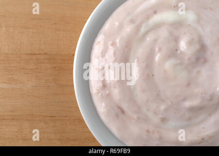 Top vista ravvicinata di una tazza di fragole e rabarbaro yogurt dolcificate con miele su una tavola di legno. Foto Stock