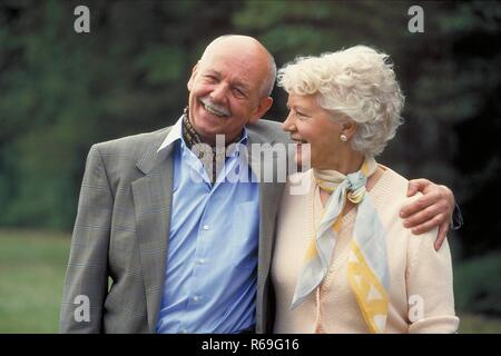 Ritratto, Halbfigur, Outdoor, ca 75 Jahre altes Seniorenpaar geht a braccetto im Park spazieren, Mann mit Schnauzbart bekleidet Hemd, Halstuch und camicia und weisshaarige Frau in gelber Kombination Foto Stock