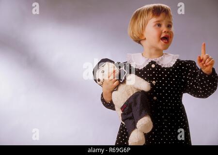 Ritratto, Halbfigur, Innenraum, 2-jaehriges bionde Maedchen bekleidet mit schwarzem, weiss getupften Kleid mit Spitzenkragen mit ihrem Kuscheltier braccio im Foto Stock