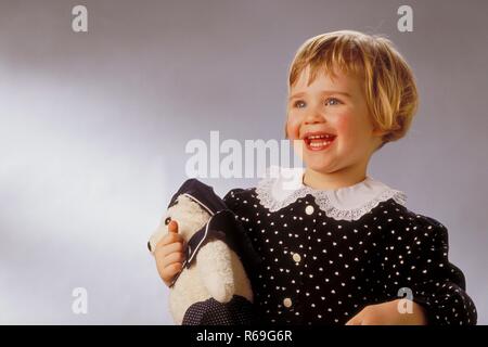 Ritratto, Halbfigur, Innenraum, 2-jaehriges bionde Maedchen bekleidet mit schwarzem, weiss getupften Kleid mit Spitzenkragen mit ihrem Kuscheltier braccio im Foto Stock