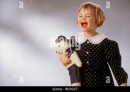 Ritratto, Halbfigur, Innenraum, 2-jaehriges bionde Maedchen bekleidet mit schwarzem, weiss getupften Kleid mit Spitzenkragen mit ihrem Kuscheltier braccio im Foto Stock