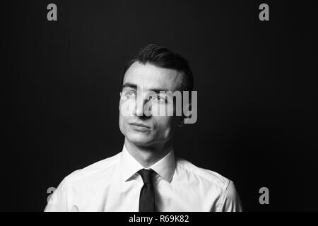 Chiudere fino in bianco e nero ritratto di un giovane uomo in camicia bianca e cravatta nera, seriamente guardando al lato, contro la pianura di sfondo per studio Foto Stock