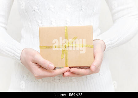 La ragazza in un maglione bianco contiene una scatola con un regalo. Foto Stock