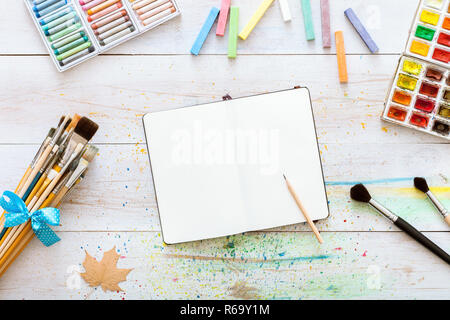 Creative Artistiche Area di lavoro Progettazione, notebook mock up per illustrazione con vernici ad acquerello, matita, set di pennelli su bianco tavolo in legno, torna a sc Foto Stock