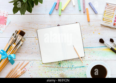 Creative concetto Workplace, in stile appartamento di design artistico tavolo, notebook vuoto mock up per la scrittura di disegno schizzi a matita, set di pennelli e tazza di Foto Stock