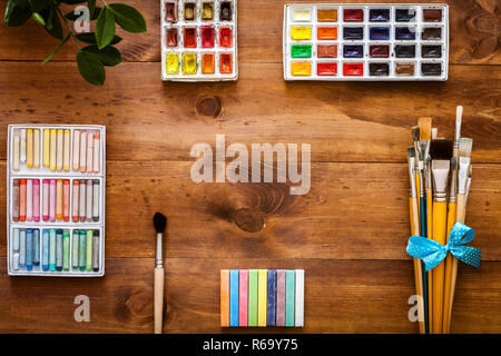 Arte creativa di lavoro gli strumenti accessori fornisce set di elementi di concetto, pennelli, paintbox con acquerelli, pastelli su legno bruno background artistico, Foto Stock