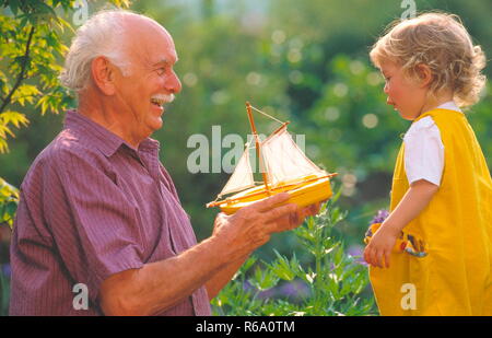 Ritratto, Grossvater gibt seinem kleinen Enkelkind ein Spielzeugsegelboot Foto Stock