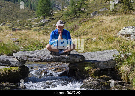 L'uomo meditando su un piccolo ponte in pietra sopra un torrente di montagna Foto Stock