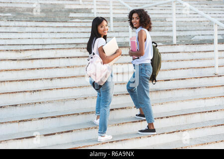 Lunghezza completa di due sorridenti studenti giovani ragazze passeggiate all'aperto, con libri Foto Stock