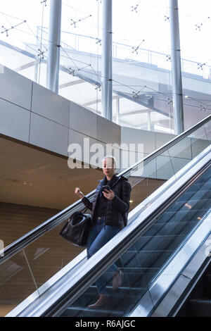 Imprenditrice con una grande borsa nera e il telefono cellulare decrescente escalator. Foto Stock