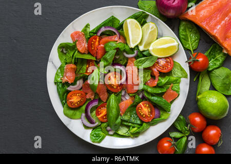 Salmone con insalata di spinaci, pomodori ciliegini, cipolla rossa e basilico in piastra di marmo scuro su sfondo di pietra. cibo sano concetto. vista superiore Foto Stock