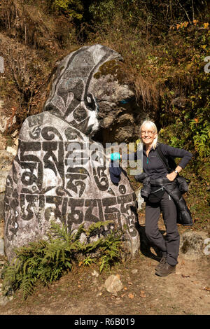 Il Nepal, Thado Koshi Gaon, senior turista femminile in posa accanto a intagliato dipinto buddista pietra Mani Foto Stock