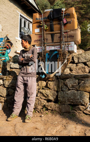 Il Nepal, Thado Koshi Gaon, giovane porter appoggiato accanto a pacco pesante sul modo di Namche Bazaar Foto Stock
