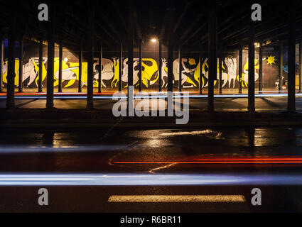 KATOWICE, Polonia - 10 Gennaio 2016: veicolare sentieri di luce sotto il ponte a Katowice nella notte. e graffiti sullo sfondo, la Polonia, l'Europa. Foto Stock