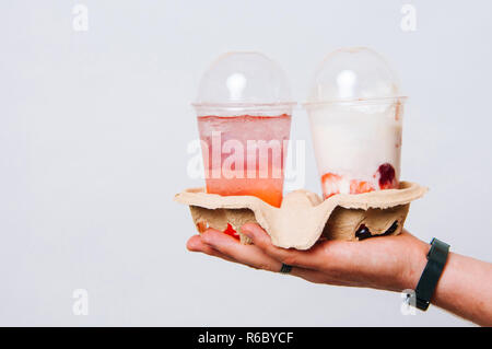 La mano di un uomo in possesso di un titolare di tazze con due tazze con Shake to go. Per andare limonata o agitare. Concetto di estate. Foto Stock