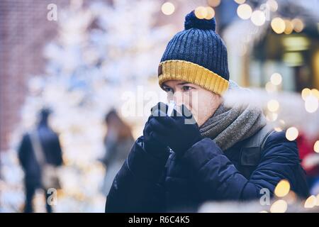Giovane uomo bevendo un vin brulé. contro illuminata di alberi di Natale. Monaco di Baviera, Germania. Foto Stock