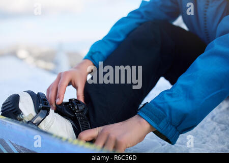 Snowboarder cinghie nelle sue gambe in scarponi da snowboard in moderno fast flow legature con cinghie. Pilota a ski resort si prepara per la sessione di freeride e . Uomo che indossa abiti alla moda. Piedi di close-up. Foto Stock