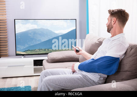 Giovane uomo con mano fratturata guardano la televisione a casa Foto Stock