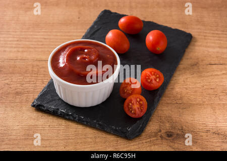 Ketchup salsa nella ciotola e pomodori sul tavolo di legno Foto Stock