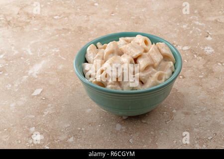 Una ciotola di pasta con carne di pollo in una salsa Alfredo su un beige chiazzato bancone. Foto Stock