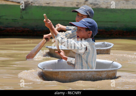 Cambogia Siem Reap, Ragazzi utilizzando una ciotola di galleggiare intorno alle barche nel lago al villaggio galleggiante di Chong Kneas, Tonle SAP Foto Stock