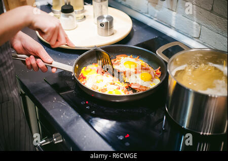 Donna mette cibo fatto in casa. Mani femminili applicato con cautela per uovo fritto piatto dal pan. La prima colazione per due persone a casa in cucina al tavolo da pranzo Foto Stock