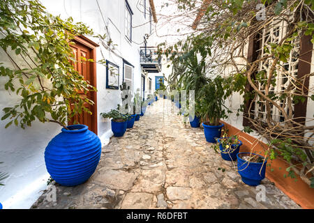 Hydra, Grecia - Ottobre 4th, 2018: una strada stretta prospettiva con blu di vasi di piante accanto alle pareti a Hydra, Grecia. Foto Stock