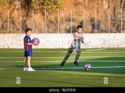 Hydra, Grecia - Ottobre 4th, 2018: due ragazzi che giocano a calcio in un campo di calcio uno di loro con la maglietta di Barcellona iin Hydra, Grecia. Foto Stock