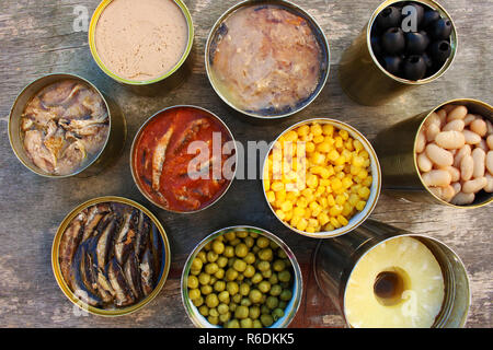 Aprire diverse conserve alimentari sul vecchio sfondo di legno. Vista dall'alto. Lay piatto. Foto Stock