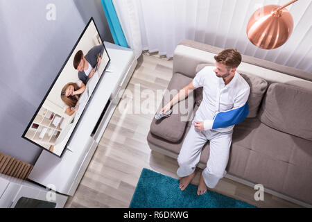 Uomo con mano fratturato di guardare la televisione Foto Stock