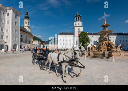 I turisti di marcia di un carro trainato da cavalli di fronte Residenzbrunnen Fontana e St Michaels chiesa sulla piazza della Residenza, Salisburgo, Austria Foto Stock