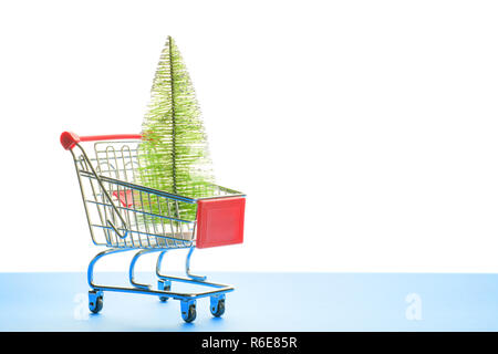 Piccolo artificiale di abete nel carrello spesa sul blu e sfondo bianco. Composizione di natale con spazio di copia Foto Stock