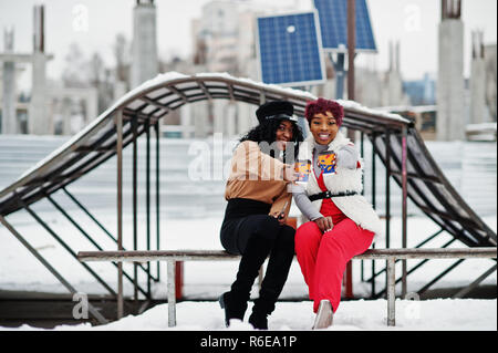 Due americano africano womans poste a giornata invernale contro sfondo innevato con tazze di caffè. Foto Stock