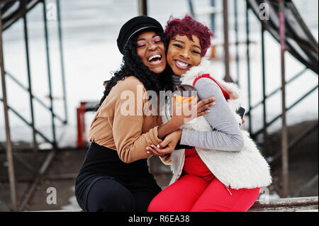 Due americano africano womans poste a giornata invernale contro sfondo innevato con tazze di caffè. Foto Stock