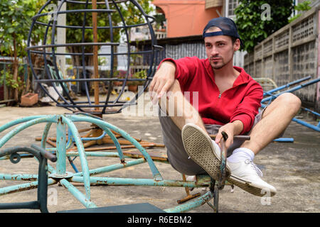 Giovane uomo barbuto pensare mentre è seduto al vecchio arrugginito merry go r Foto Stock