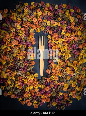 La pasta a spirale multicolore di farina di frumento su uno sfondo nero e legno forcella Foto Stock