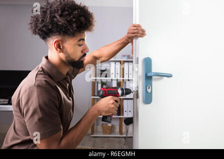 Carpenter Installazione serratura della porta con un cacciavite senza fili Foto Stock