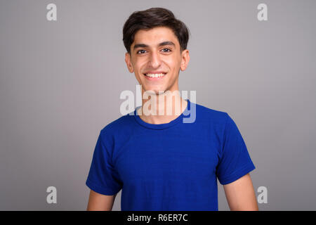 Giovani felici persiano di ragazzo adolescente sorridente contro uno sfondo grigio Foto Stock