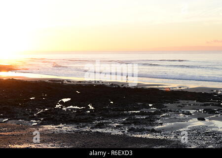 Lone surfer sulla spiaggia rocciosa all'alba Foto Stock