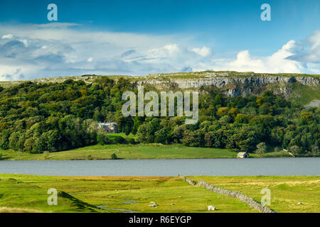 Vista pittoresca su Malham Tarn (lago glaciale) bosco & torreggianti scogliere calcaree sotto il profondo blu del cielo - Malhamdale, Yorkshire Dales, Inghilterra, Regno Unito. Foto Stock