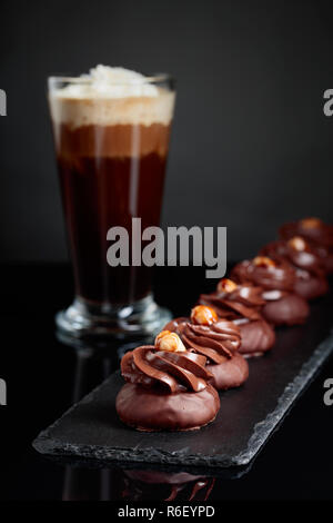 Dolce al cioccolato con granella di nocciole e caffè con panna su un nero sfondo riflettente. Foto Stock