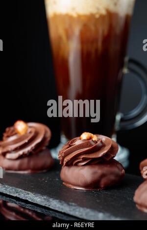 Dolce al cioccolato con granella di nocciole e caffè con panna su un nero sfondo riflettente. Foto Stock