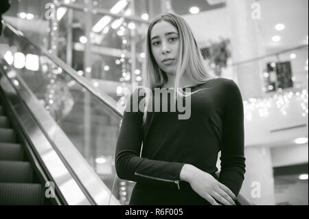 Ragazza in un abito nero va sulla scala mobile al centro commerciale Foto Stock