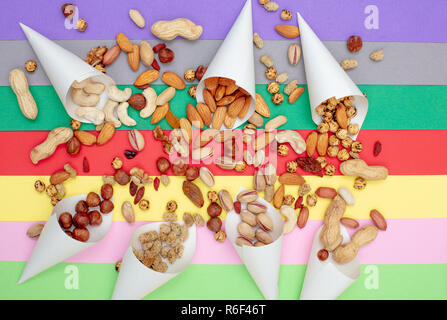 I dadi assortiti servito in coni di carta sparsi su un colorato sfondo della carta vista superiore Foto Stock
