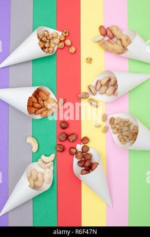 I dadi assortiti servito in coni di carta sparsi su un colorato sfondo della carta vista superiore Foto Stock