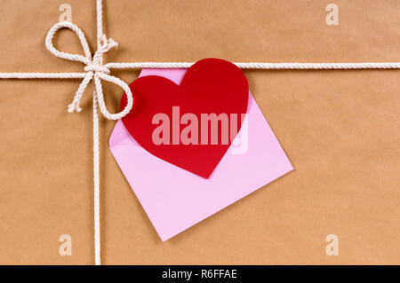 Il giorno di San Valentino regalo con forma di cuore card o tag regalo, marrone confezione di carta pacco sfondo, spazio di copia Foto Stock