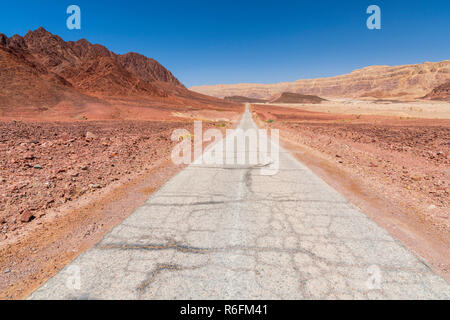 Strada lastricata che corre attraverso il deserto di Arava tra monti rossi a Timna Parco Nazionale, Israele Foto Stock
